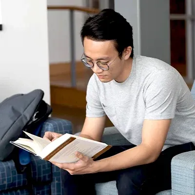 Male college student sitting in chair reading textbook